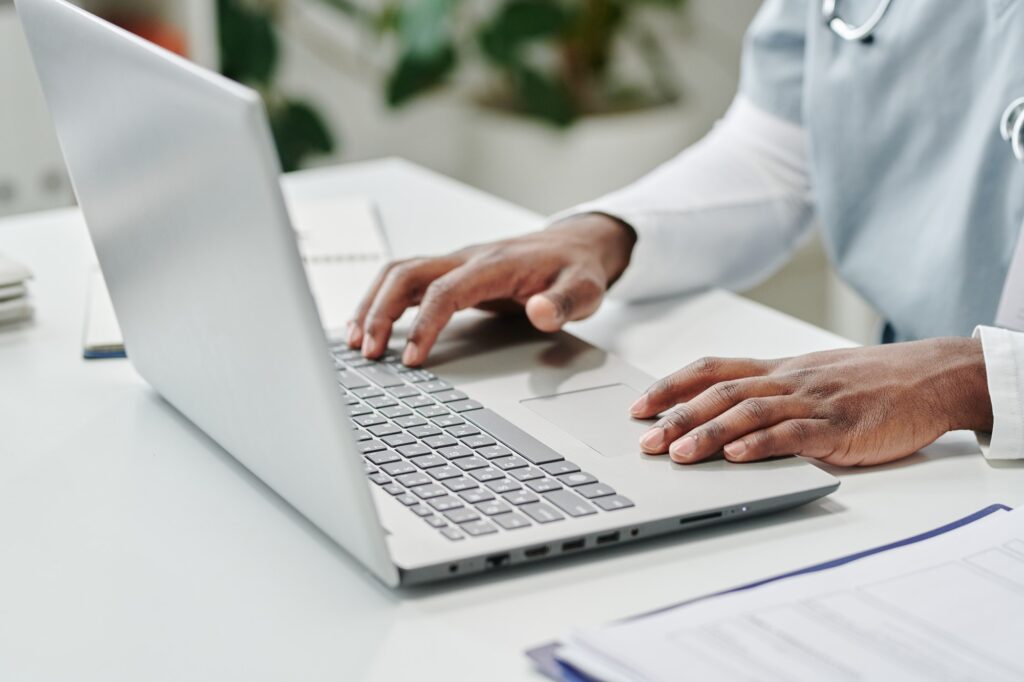 Hands of young African American male online doctor sitting in front of laptop