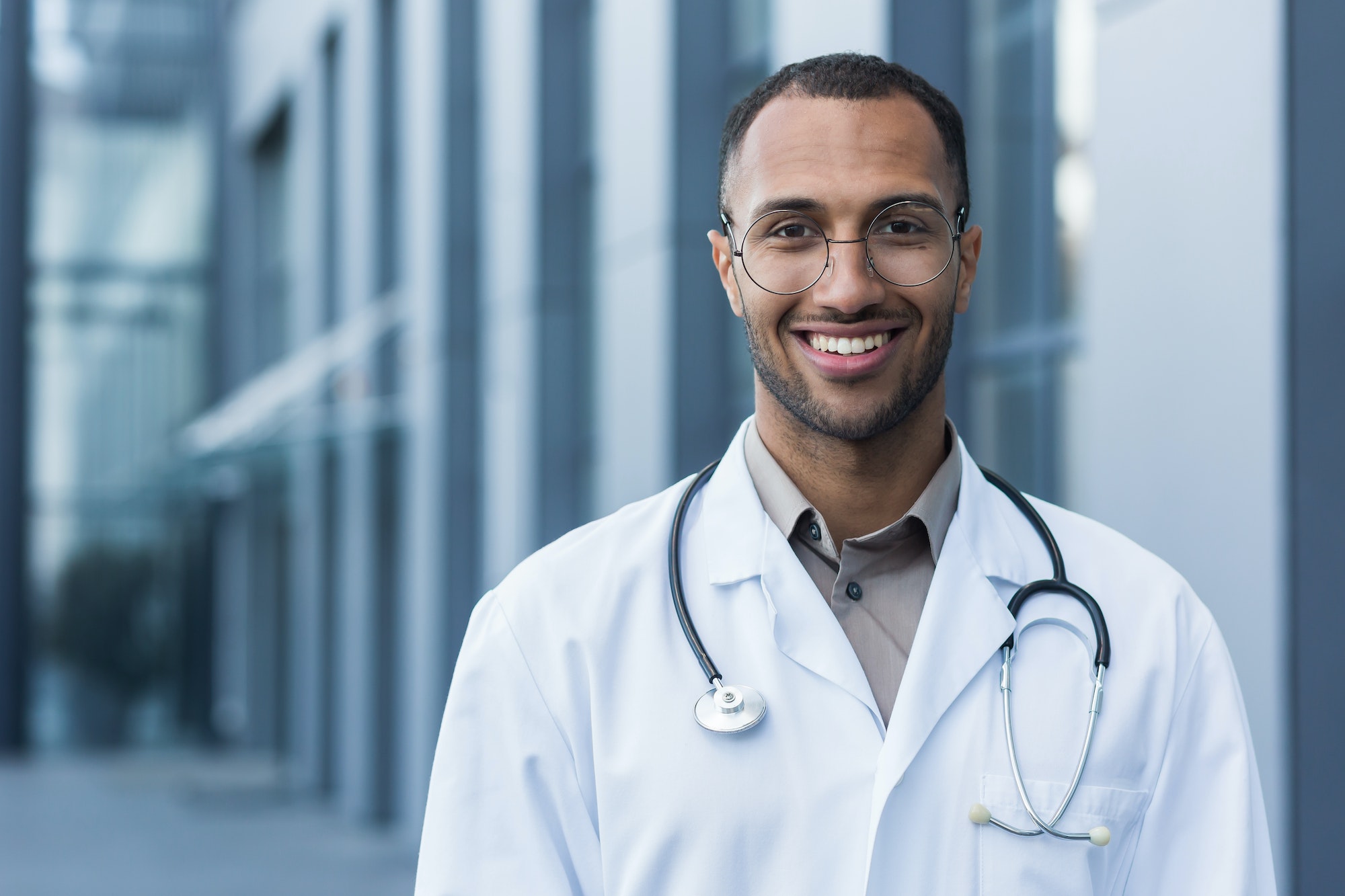 Close-up photo portrait of young African American doctor outside hospital, man in medical coat